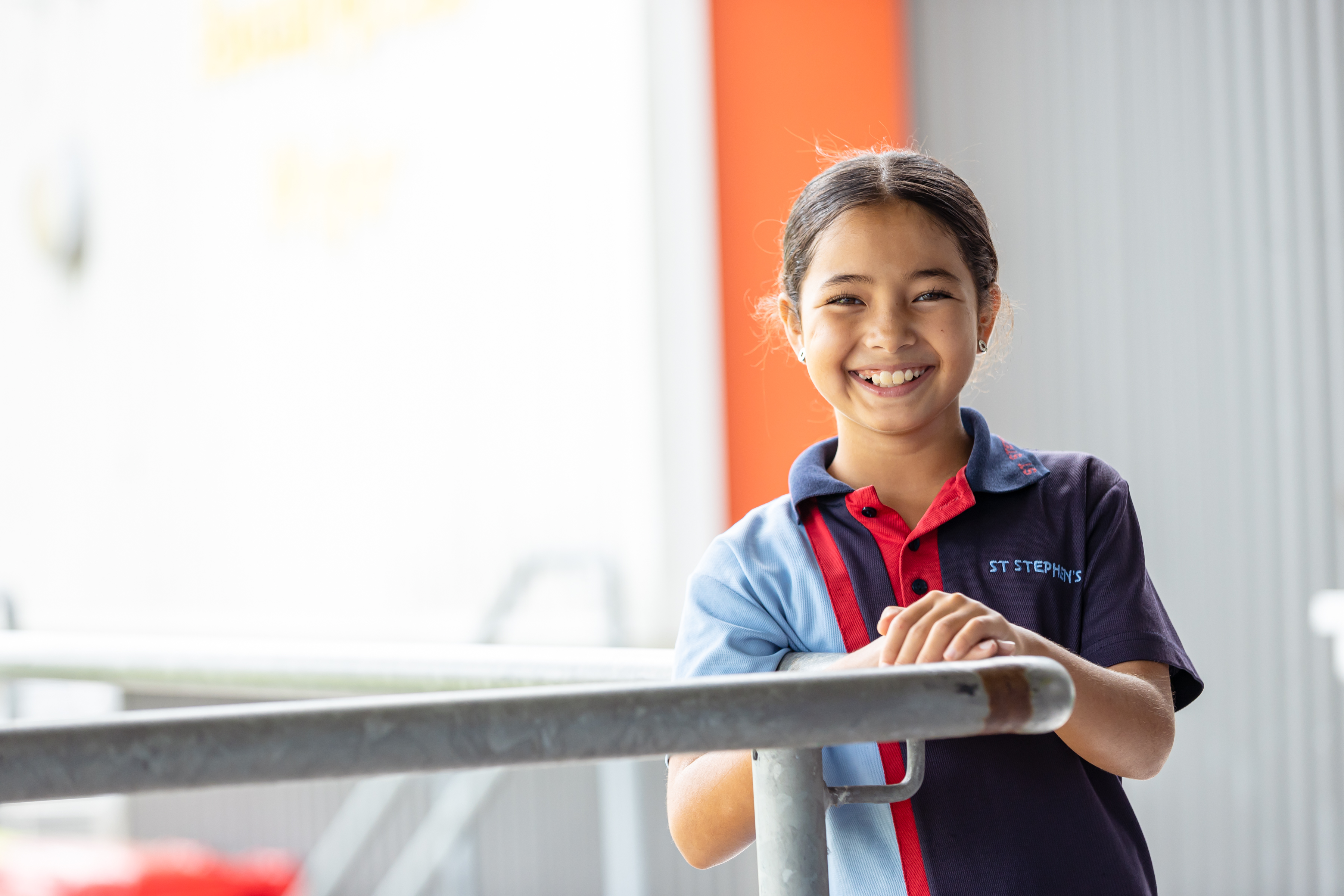 A student holding on to a railing. She is faced towards the camera and smiling.